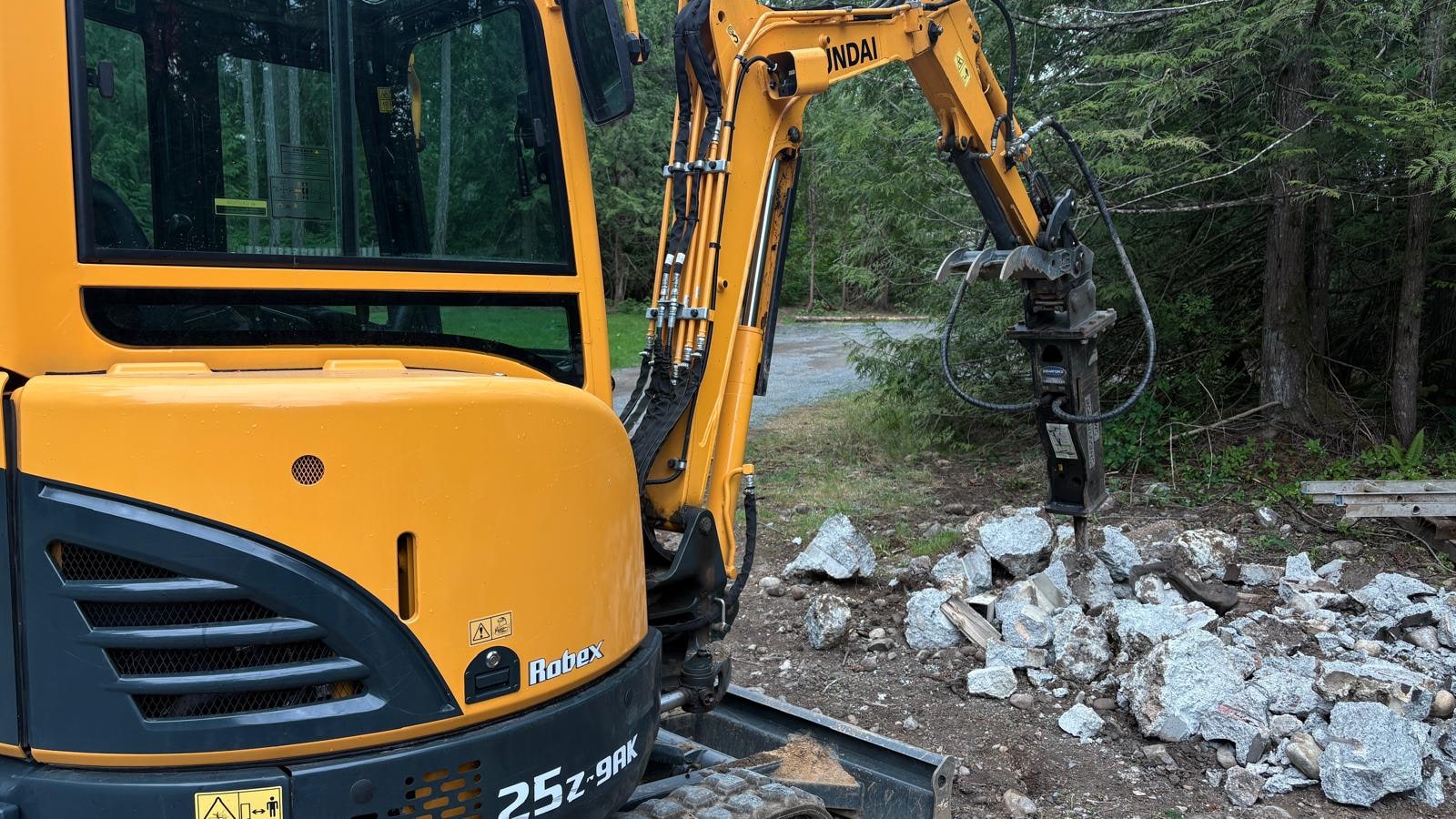 Mini excavator with hammer attachment breaking rock and concrete